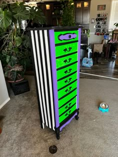 a purple and green cabinet sitting on top of a floor next to a potted plant