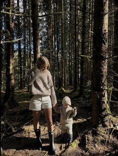 a woman and child are walking through the woods