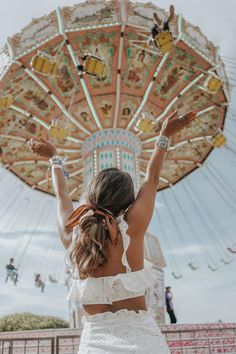 a woman standing in front of a carnival ride with her arms up and hands behind her back