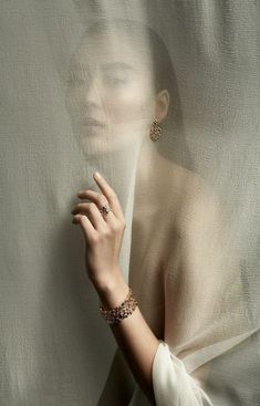 a woman with her hand on the sheer curtain behind her head, wearing an animal print bracelet