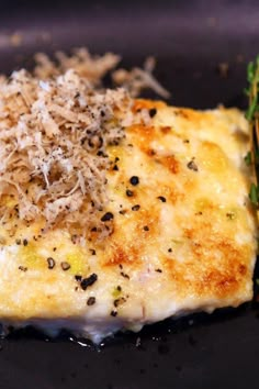 a piece of food on a black plate with parmesan sprinkles