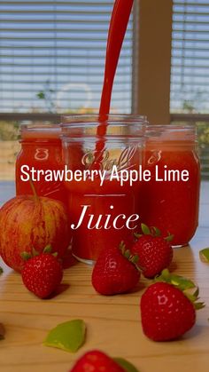 three jars filled with liquid sitting on top of a wooden table next to strawberries