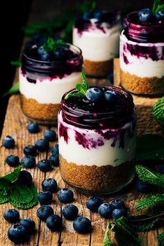 three jars filled with blueberry cheesecakes on top of a wooden table next to mint leaves