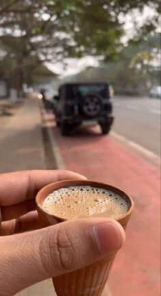 a person holding up a cup of coffee in front of a black truck on the road