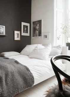 a bedroom with black walls and white bedding, pictures on the wall above the bed