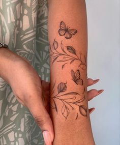 a woman's arm with butterflies and leaves on it, as if she is holding something in her hand