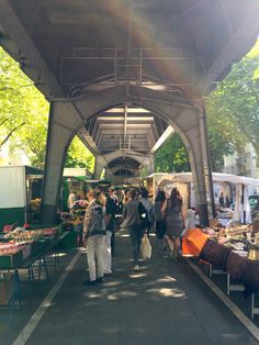 people are walking under an overpass with many tables full of food and produce on display