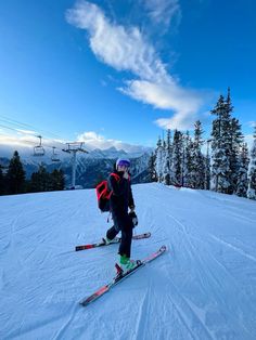 a person riding skis on top of a snow covered slope with trees in the background