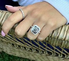 a woman's hand wearing a ring with the letter d on it, sitting next to a wicker chair