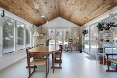 an empty dining room with wooden ceiling and windows overlooking the backyard area in wintertime