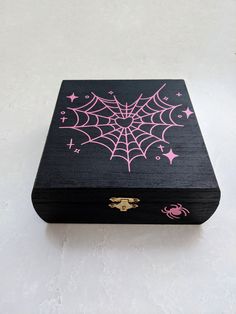 a black box with pink spider web designs on the front and sides, sitting on a white surface