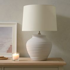 a white lamp sitting on top of a wooden table next to a framed photo and a candle