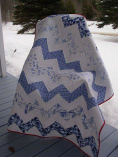 a blue and white quilt sitting on top of a wooden porch next to snow covered trees