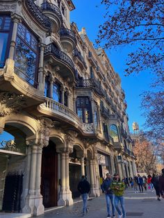 people are walking down the sidewalk in front of an ornate building with many windows and balconies