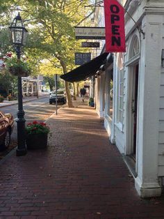 an empty sidewalk in front of a store with a red sign hanging from it's side