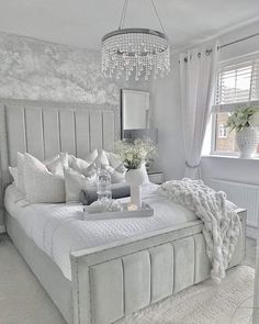 a white bedroom with a chandelier hanging from the ceiling and pillows on the bed