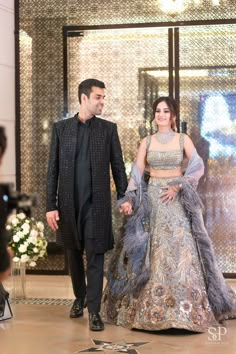 a man and woman in formal wear walking down the runway together, dressed in evening gowns