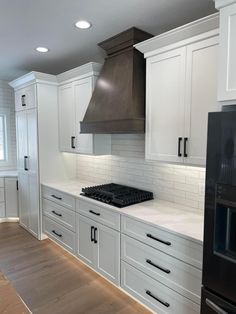 an empty kitchen with white cabinets and black stove top oven in the center, along with wooden flooring