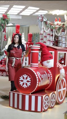 a woman in an apron standing next to a fake coca - cola train and christmas decorations