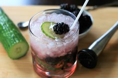 a drink with blackberries and cucumber on the side next to a pickle