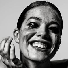 a black and white photo of a woman with makeup smeared on her face, smiling