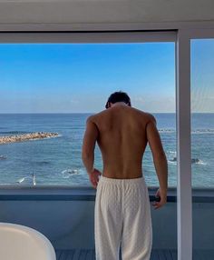 a man standing in front of a window looking out at the ocean