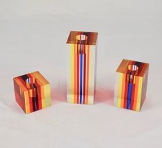 three pieces of art made out of different colored boxes on a white tableclothed surface