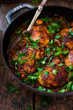 a skillet filled with chicken and lentils on top of a wooden table next to a fork