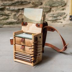 a wooden box with drawers and leather straps on the front, sitting on concrete floor