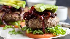 two hamburgers with lettuce, tomato and avocado on them sitting on a plate