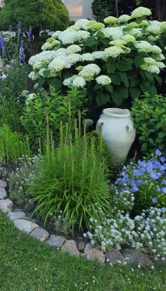 a white vase sitting in the middle of a garden filled with lots of flowers and plants