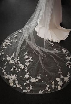 a wedding veil with white flowers on the bottom is seen from above as it sits on a black surface