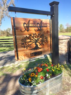 a wooden sign sitting next to a metal tub filled with flowers and plants on top of a grass covered field