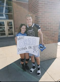 two people standing next to each other holding a sign that says what oreo doing on set?