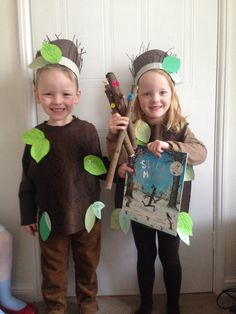 two children dressed up in costumes standing next to each other holding sticks and paper leaves