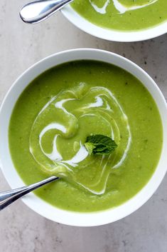 two bowls filled with green soup on top of a table