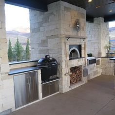 an outdoor kitchen with stone fireplace and grilling area next to large open patio doors