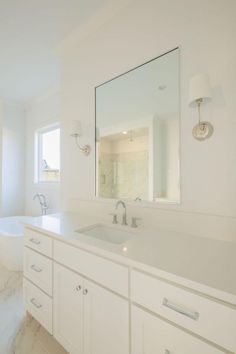 a white bathroom with marble counter tops and large mirror over the bathtub, along with two sinks