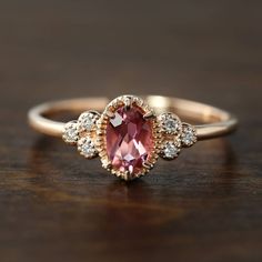 an oval shaped pink sapphire and diamond ring on top of a wooden table with white diamonds