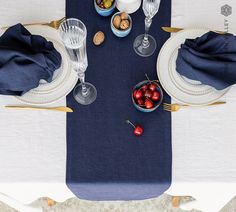 the table is set with blue linens and gold placemats, plates, silverware, and cherries