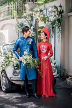 a man and woman standing next to each other in front of a car with flowers on it