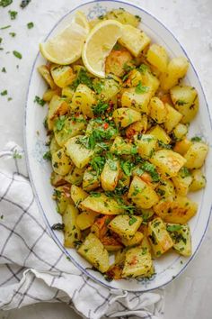 a white plate topped with potatoes covered in herbs and lemon wedges next to a napkin