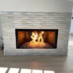 a fire is burning in a fireplace with white tiles on the wall and wood floor