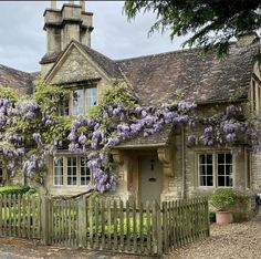 a house with purple flowers growing on it's side and a wooden fence in front