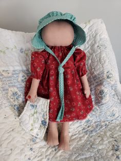 a doll with a red dress and green bonnet is sitting on a bed