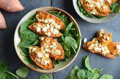 two bowls filled with spinach, feta cheese and sweet potato halves next to some other vegetables