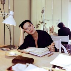 a woman sitting at a table with an open book in front of her and a lamp above her