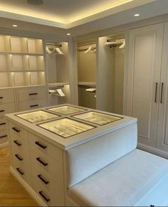 an empty walk - in closet with white drawers and glass shelves on the wall, along with a bench