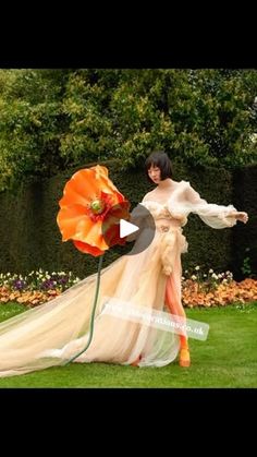 a woman in a long dress holding an orange and white umbrella while standing on grass