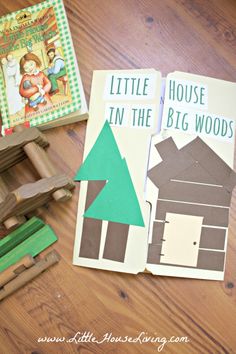 two children's books sitting on top of a wooden table next to a toy house